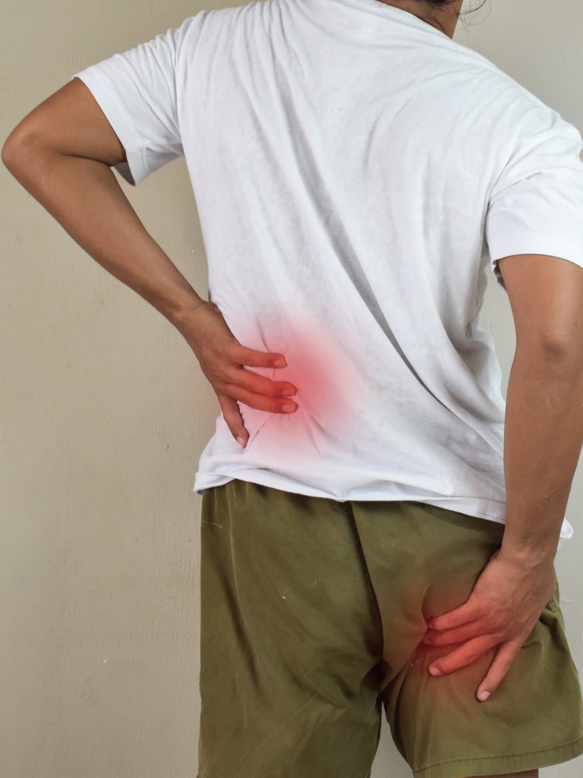 A person holding both their lower back and hip, with the two areas of pain highlighted in red showing a radiating pattern.
