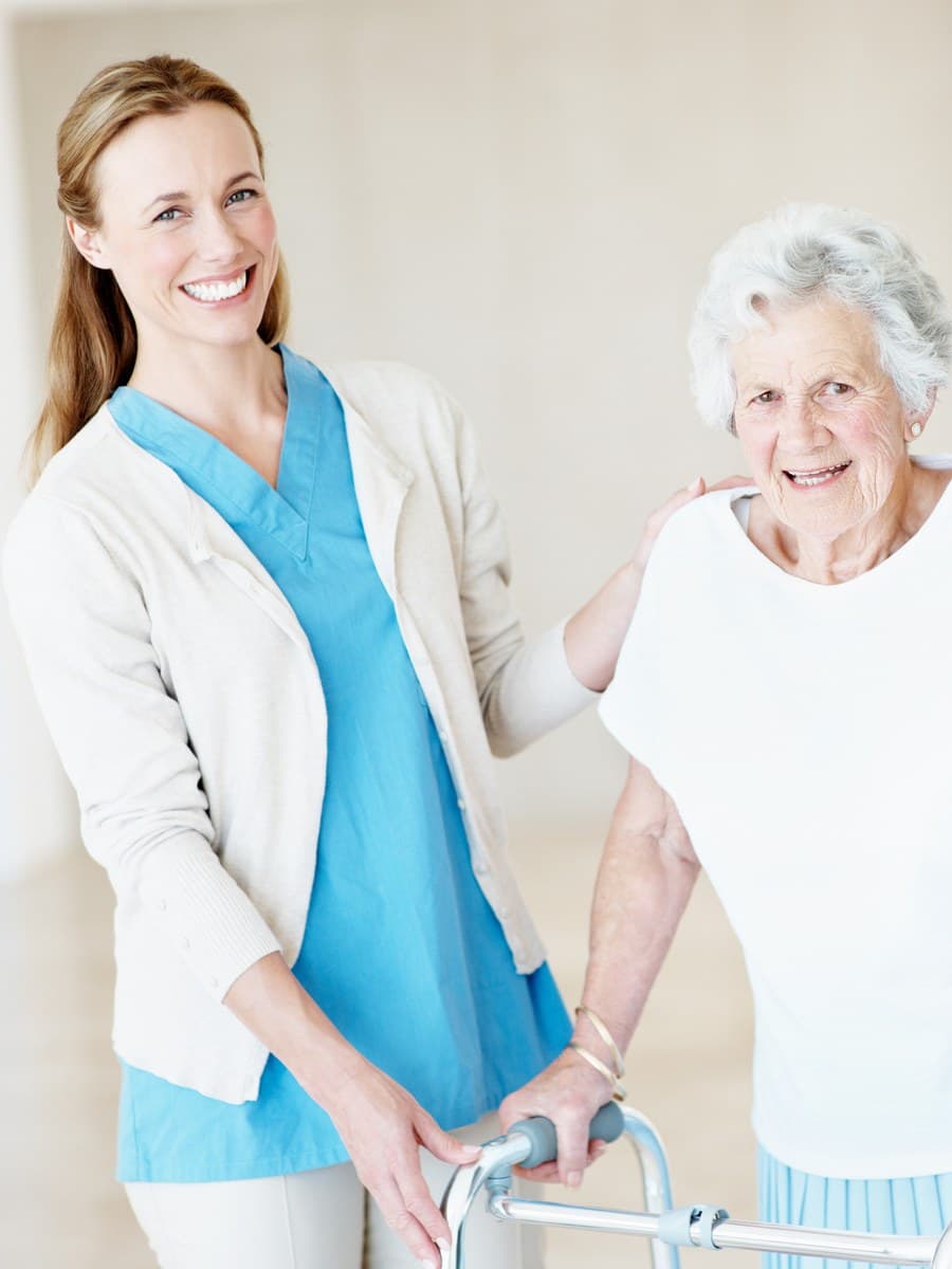 A caregiver helping an elderly woman walk using a walker.