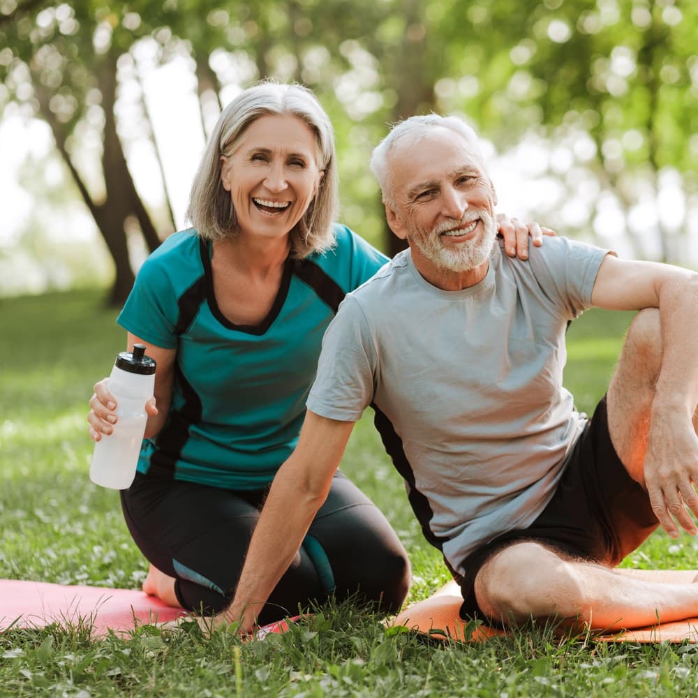 A smiling senior couple relaxing on yoga mats outdoors after exercising together.